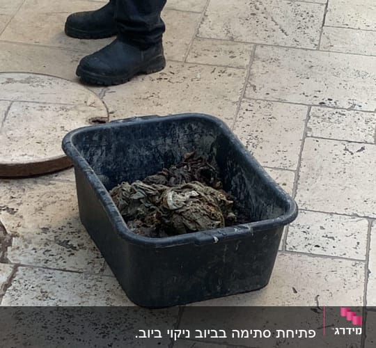 אדם עומד ליד פתח ביוב עם דלי פסולת